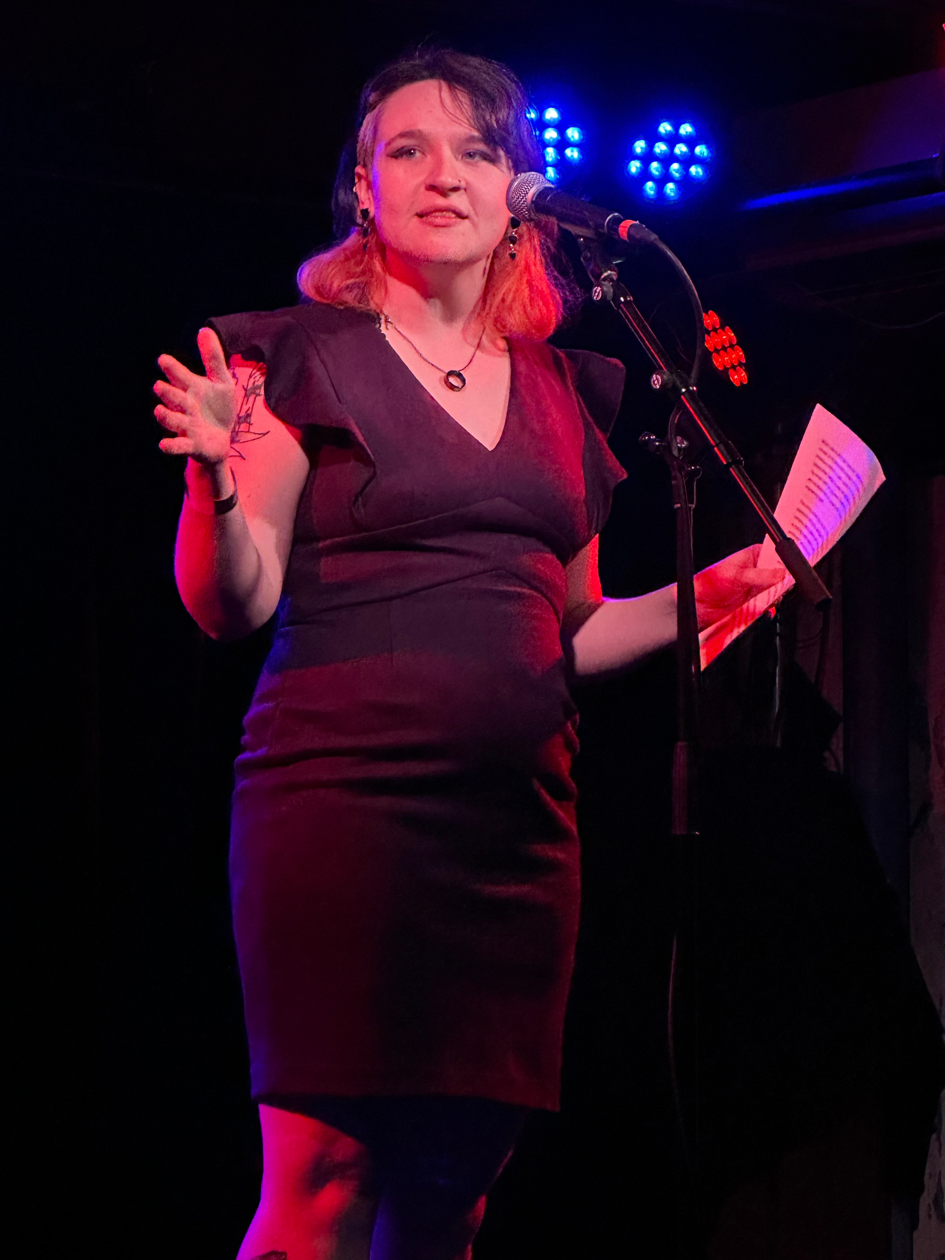 Joley holds a script and stands at a microphone in a purple dress